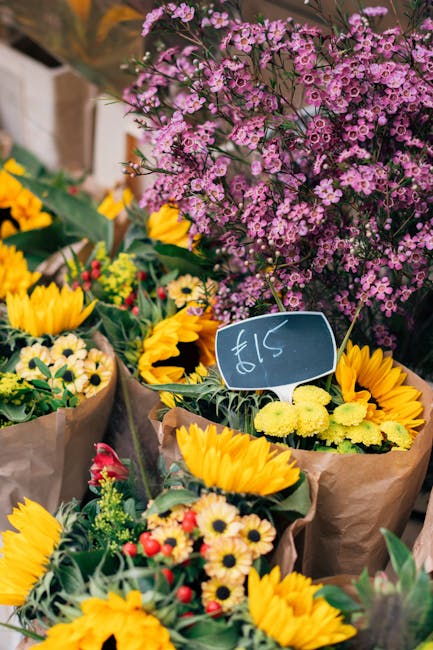A vibrant display of fresh flower bouquets arranged for flower delivery, featuring bright yellow sunflowers, small white daisies with yellow centers, and red and pink roses, all wrapped in brown paper