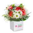 Like a breath of fresh air in the heart of New Malden, this exuberant bouquet glows with health and happiness, nestled within an immaculate square white gift bag. The composition is a cheerful blend: coral and peach carnations, their many-petalled forms ruffled and inviting, share space with pristine white daisies and their striking greenish-yellow centers, infusing the arrangement with lightness and vitality. Baby's breath drifts delicately among the blooms, its tiny white blossoms lending an ethereal, uplifting effect, while just beside them, a few purple-edged buds quietly rest, hinting at a new chapter soon to unfold. Everything is encased in abundant, dark green foliage, the wide glossy leaves fanning out to frame the rounded design in a lush embrace. The clean, functional white bag, trimmed with smooth ribbon handles, completes the presentation, making the bouquet appear both gift-ready and personal-a perfect reflection of the New Malden community's spirit, whether it's to mark a celebratory event on Kingston Road or to offer encouragement nearby Motspur Park. With every careful flourish and fresh detail, the arrangement invites joy and gratitude, expressing the timeless art of local floristry at Flowers New Malden.